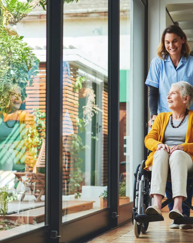 Personne âgée en fauteuil roulant aidée par une infirmière